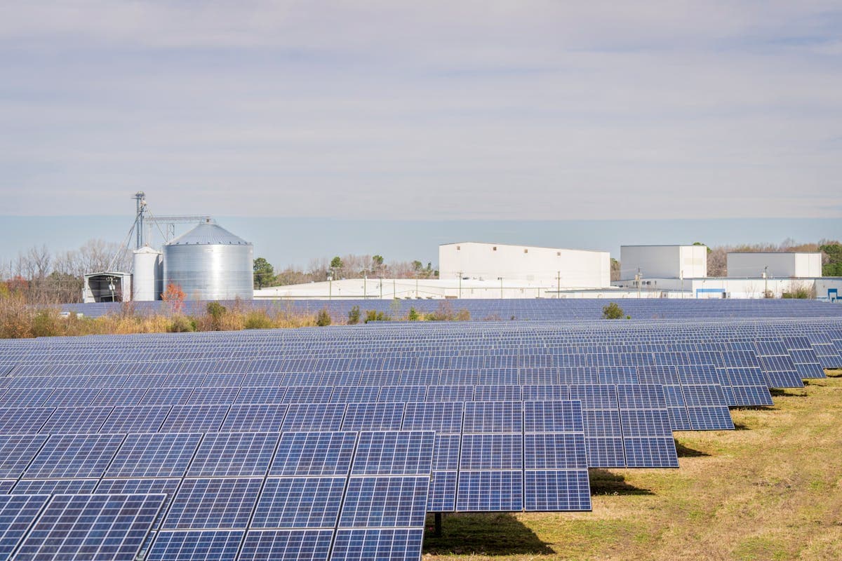 Solar panel field with agricultural buildings under a clear sky